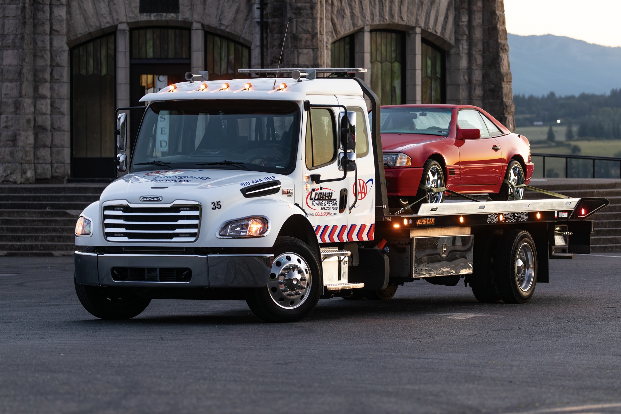 Crown Freightliner flatbed tow truck transporting a red Mercedes SL convertible