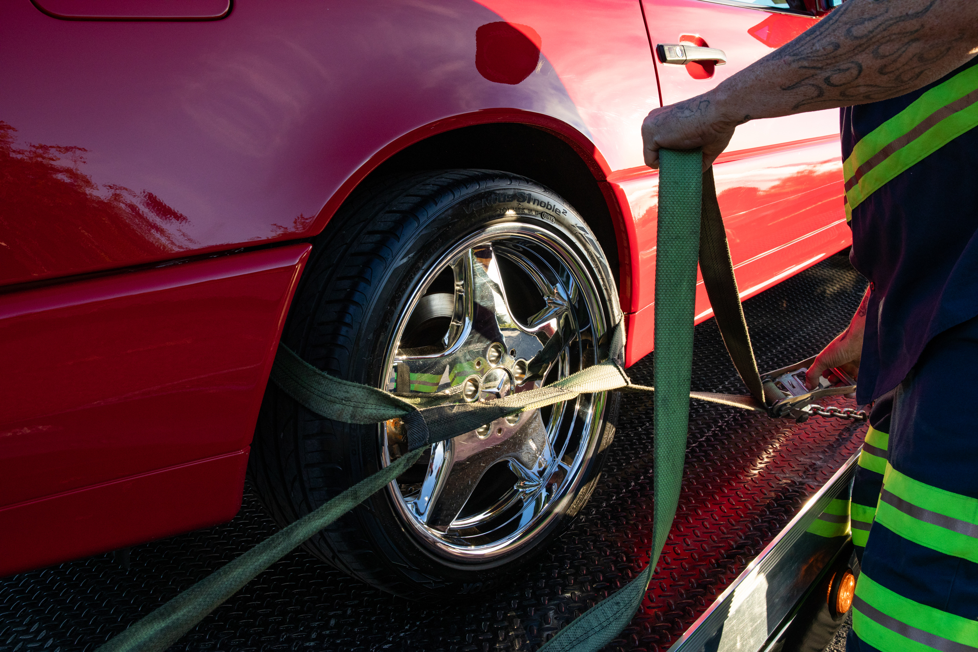 Crown tow operator securing a red sports car's front wheel with straps on the flatbed