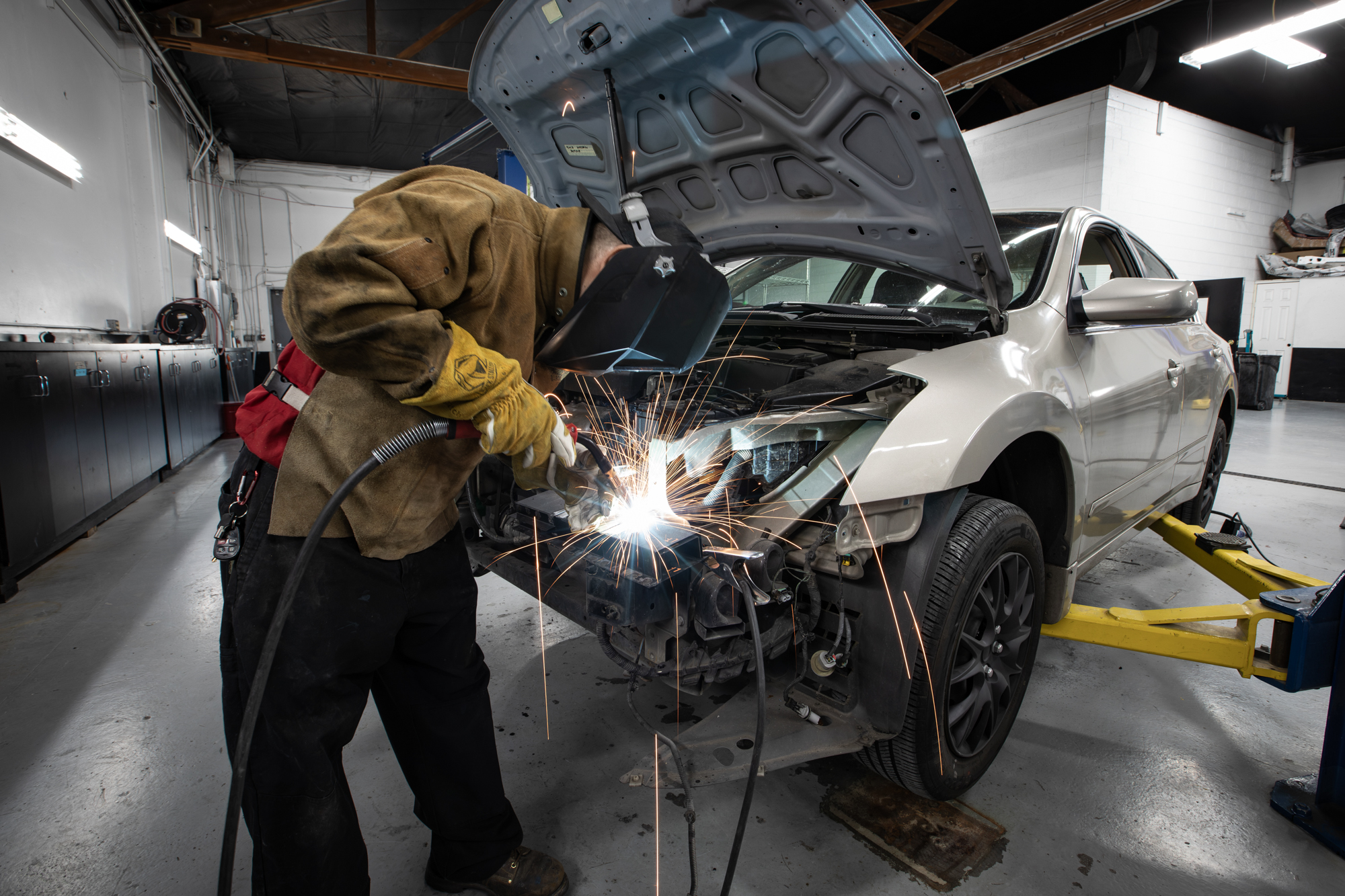 Crown technician MIG welding front-end structural repair on a sedan